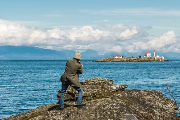 Man photographing Entrance Island Lighthouse from Orlebar Point, Gabriola Island