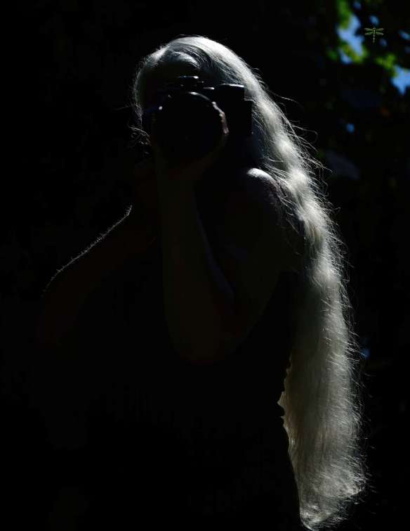 Dark image of woman with long hair, holding camera up to her eye