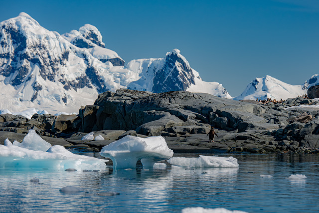 Icebergs along the shore with sharp, snow-covered peaks in the background.